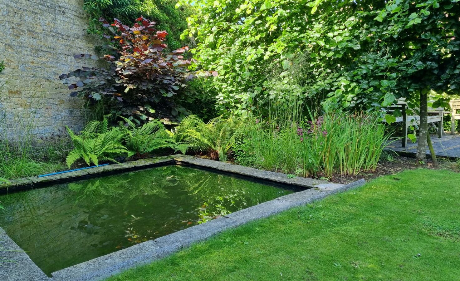 Beautiful cottage garden surrounding a historic property, featuring lush, colorful planting, mature trees, vibrant flower borders, sweeping feature lawns, and a large ornamental water feature. Traditional English garden design blending heritage charm with natural landscaping and timeless countryside elegance.